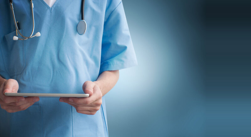 Pflegekraft in blauer Arbeitskleidung hält Tablet Computer. Symbol für conalliance, advisory, special care, care, transaction, Berater, Beratung, Mergers, Acquisitions, M&A, Unternehmensverkauf. Fokus auf Health Care.